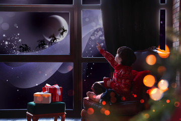 Cute little boy waiting for Santa Claus near window at home. Christmas holiday - Powered by Adobe