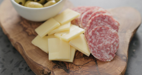 green olives, cheese and salami on olive wood board