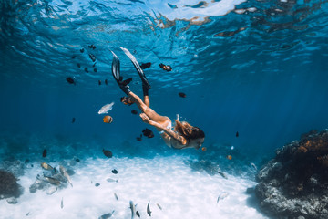 Freediver girl with fins glides over sandy bottom with fishes in blue ocean - obrazy, fototapety, plakaty