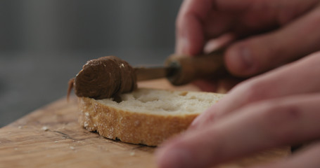 man spreading chocolate nut butter on ciabatta slice on olive board