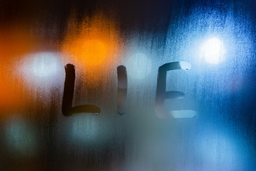 the word lie written on night wet window glass close-up with bokeh background