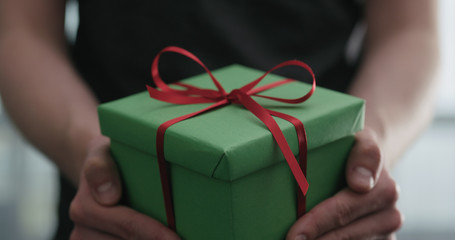 young man shows green paper gift box with red ribbon