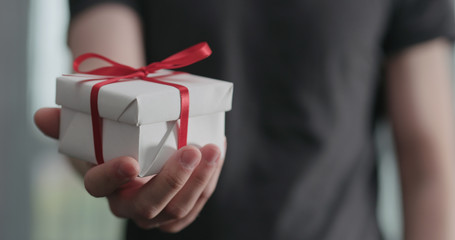 young man shows white paper gift box with red ribbon