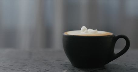 cappuccino with marshmallow in black cup on terrazzo countertop