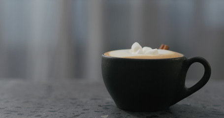 cappuccino with marshmallow and cinnamon in black cup on terrazzo countertop