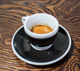 A small cup of freshly made espresso on a dish on a large table