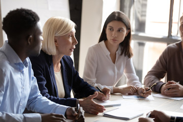 Confident older female boss team leader talking to focused workers.