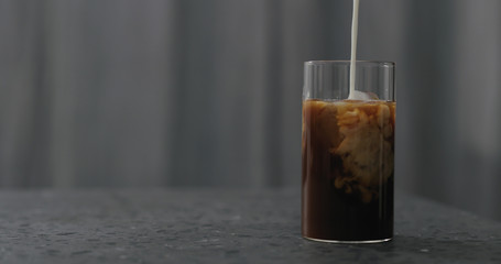 pour milk into iced coffee on terrazzo countertop