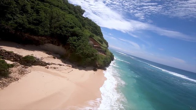 FPV drone footage following the coastline of Gunung Payung Beach in Bali, and then coming inland to showcase the vibrant greenery, Indonesia 