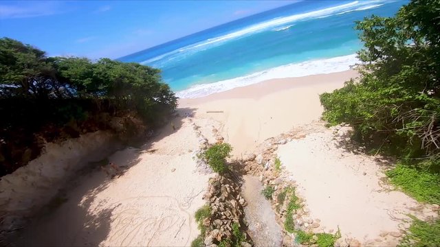 FPV drone footage of vibrant greenery that dips to the sand of a beach, before tilting back to reveal the blue sky, Bali, Indonesia 