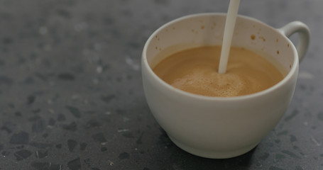 pouring steamed milk into cappuccino in white cup on terrazzo countertop