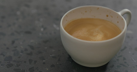 pouring steamed milk into cappuccino in white cup on terrazzo countertop