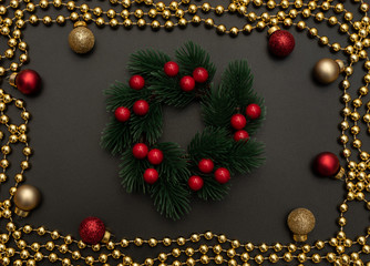 Christmas black background with Christmas wreath with berries, golden beads and red and golden Xmas decorations. Flat lay style. New Year greeting card.