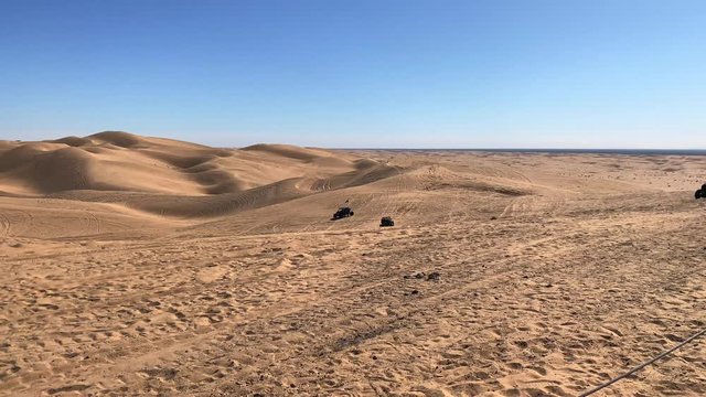 Pan view of ATVs driving on sand dunes, on a sunny day, in USA
