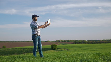 A farmer in a green barley field in spring makes the photo with a digital tablet, uses tablet. The concept of increasing yields, healthy food in agriculture and the use of digital technology
