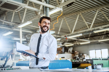 Handsome smiling caucasian bearded graphic engineer holding notebook while standing in printing...