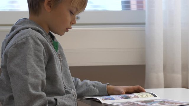 Static shot of a kid reading a comic book, in a classroom, at a elementary school, in Finland