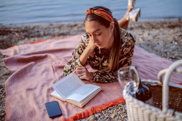 Attractive caucasian brunette in floral dress and with headband lying on stomach on blanket on the...