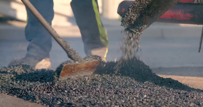 Paving machine distributes hot asphalt onto the road while workers spread it out