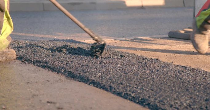 Construction worker is spreading the newly poured asphalt onto the street