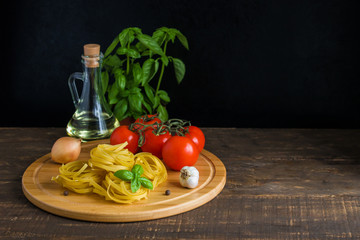 raw fettuciine pasta fresh tomatoes basil olive oil garlic onion on cutting board wooden table copy space