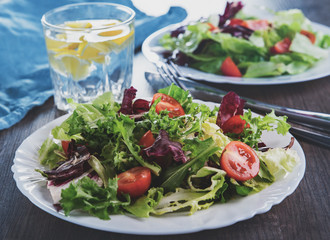 various fresh mix salad leaves with tomato in white plate on wooden background