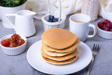 Pancakes with blueberries, cherries and mini apple jam. A cup of coffee and gravy boat in the background. Traditional american pancakes. Close-up.