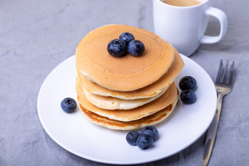 Pancakes with blueberries. A cup of coffee in the background. Traditional american pancakes. Close-up.