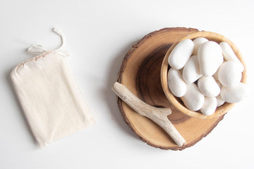Mock up of cotton bag or pouch and bowl with white pebble and wooden cut tree section on white...