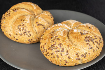 Group of two whole sesame kaiser roll on gray ceramic plate on grey stone
