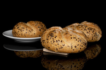 Group of three whole sesame kaiser roll on white ceramic plate on wooden cutting board isolated on black glass