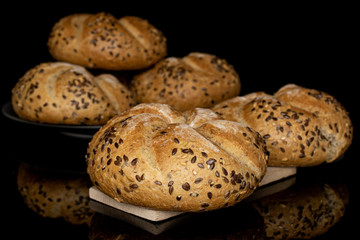 Group of five whole sesame kaiser roll on gray ceramic plate on wooden cutting board isolated on black glass