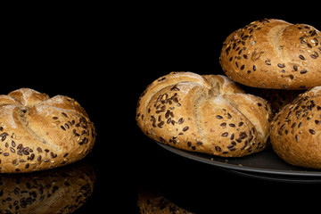 Group of four whole sesame kaiser roll on gray ceramic plate isolated on black glass
