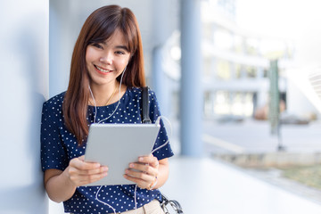 Happy young asian woman smiling at camera while listening to a podcast or music from her tablet computer