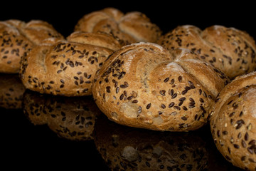 Group of six whole sesame kaiser roll isolated on black glass