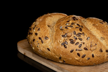 One whole sesame kaiser roll on bamboo cutting board isolated on black glass