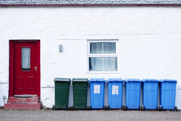 Blue green coloured wheelie bins in a row outside house waiting for bin men to collect oil rural countryside UK