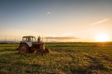 Red tractor on golden sunset sky.