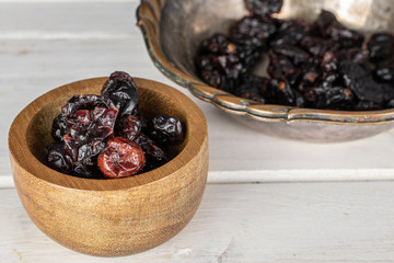 Lot of whole dried cowberry................ in copper bowl in bamboo bowl on white wood