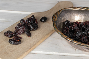 Lot of whole dried cowberry................ in copper bowl on wooden cutting board on white wood
