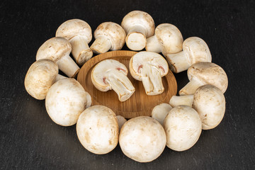 Group of lot of whole two halves of fresh white champignon on round bamboo coaster on grey stone