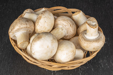 Lot of whole fresh white champignon in round rattan bowl on grey stone