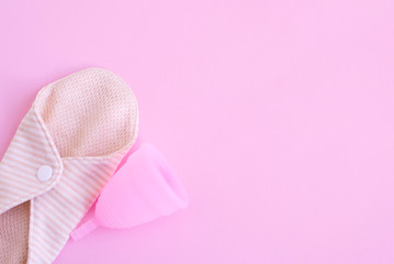 reusable pad and pink menstrual cup on pink background. woman period concept. eco friendly flat lay.