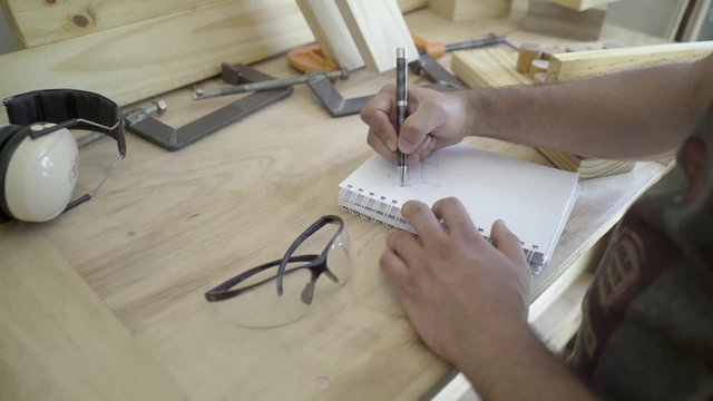 Carpenter sketches draws diagram plans at his workbench before starting a project