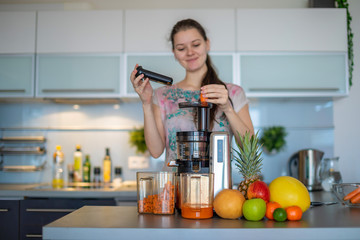 Woman making fruit juice using juicer machine in home kitchen, healthy eating lifestyle concept