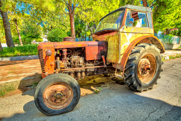 Side view of an old yellow vintage tractor with broken wheel abandoned in an old street.