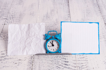 Mini blue alarm clock standing above buffer wire between two notation paper