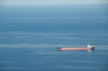 Blue seascape with calm waters and cargo vessel in the foreground. Dry-cargo ship at anchorage not far way from seashore