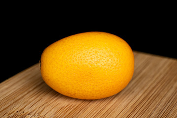 One whole tasty orange kumquat on bamboo cutting board isolated on black glass