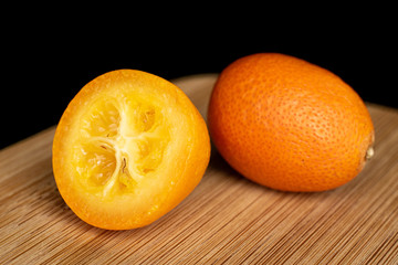 Group of one whole one half of tasty orange kumquat on bamboo cutting board isolated on black glass